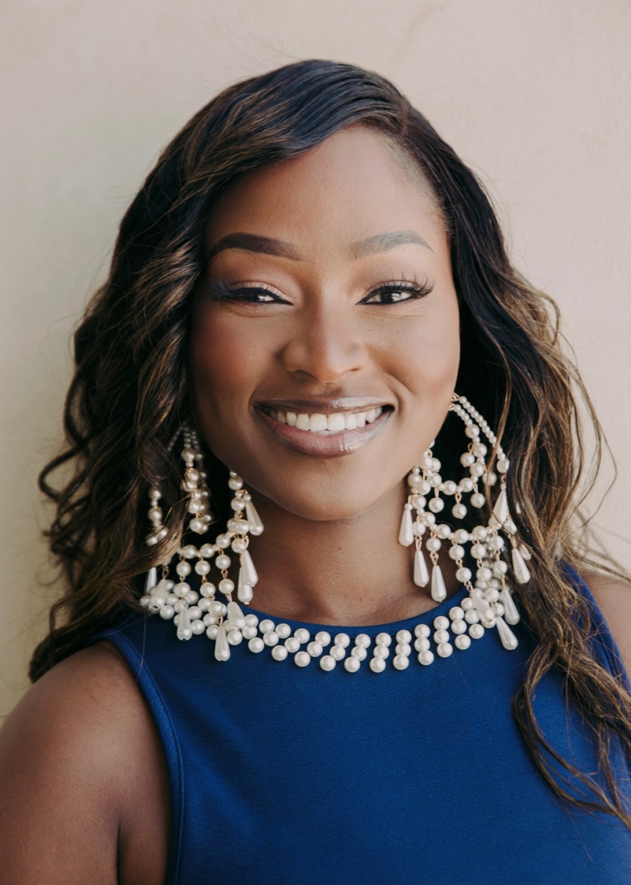 Ejiro Obayomi in a blue dress with statement pearl earrings, smiling