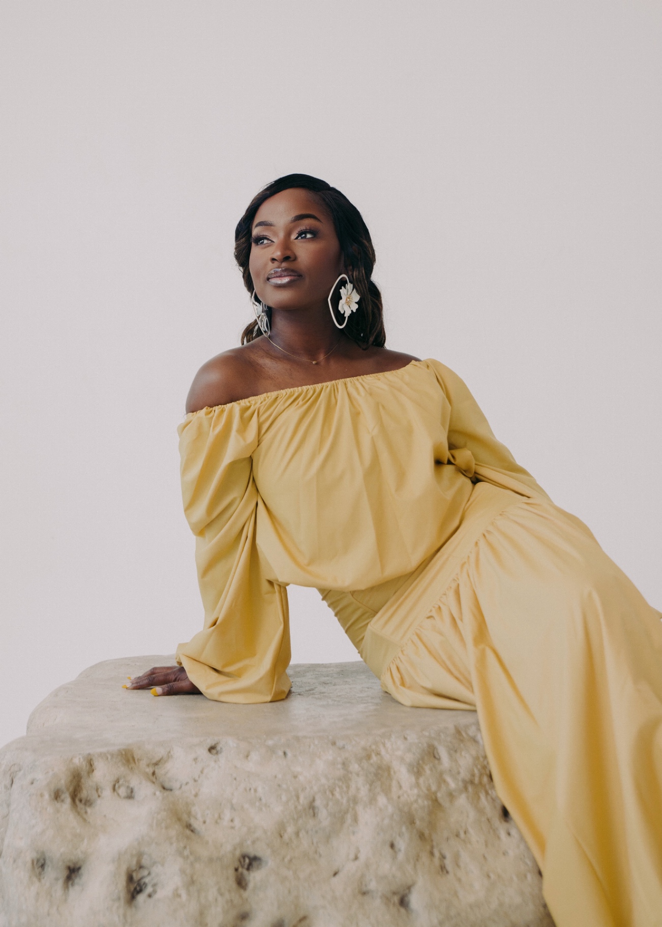 Ejiro Obayomi posed in a yellow dress on a stone pedestal
